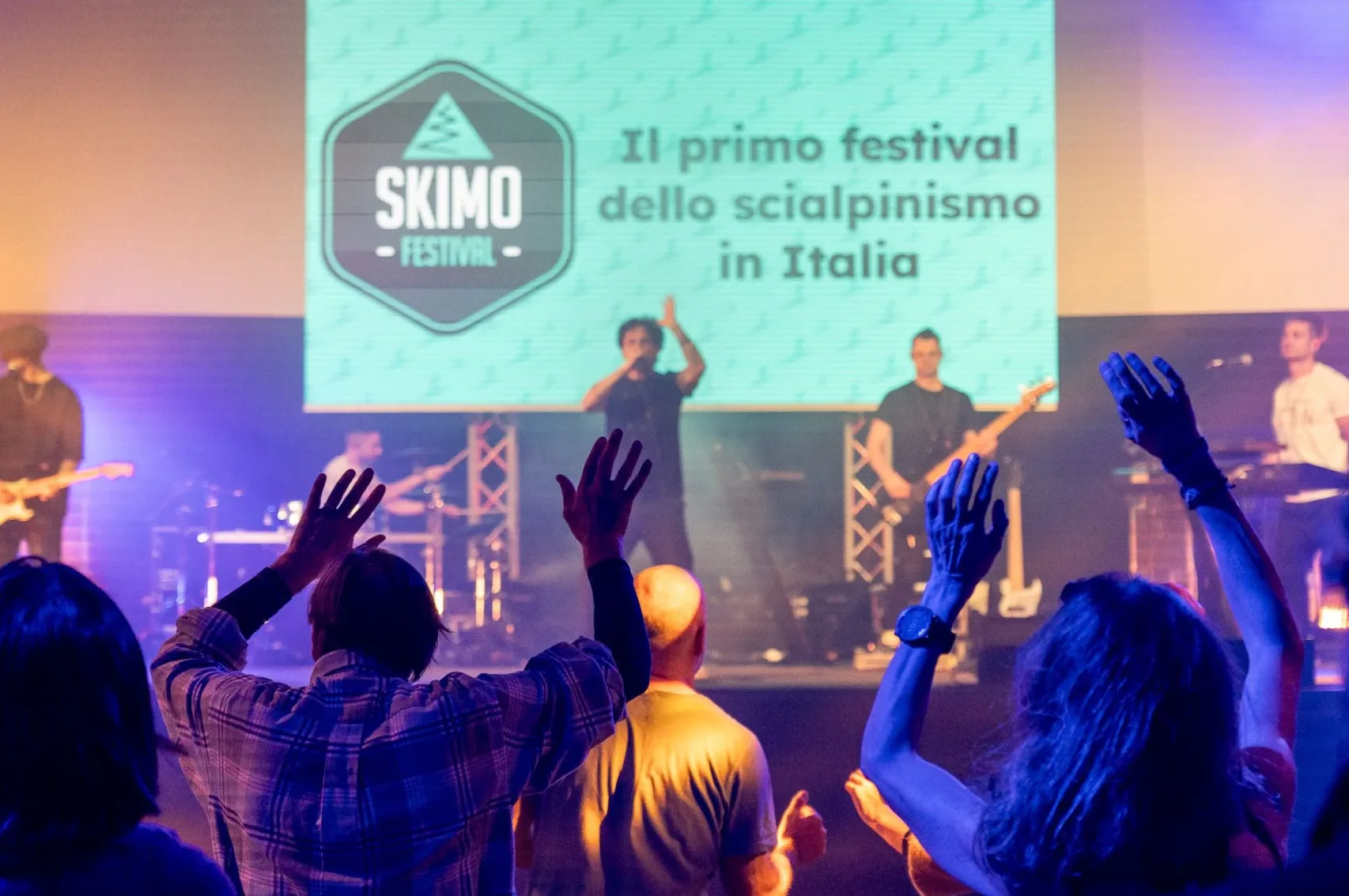 Audience watching a live band at Skimo Festival, with the festival logo on the stage screen